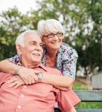 man sitting on bench with wife hugging him from behind