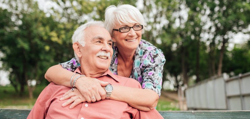 man sitting on bench with wife hugging him from behind