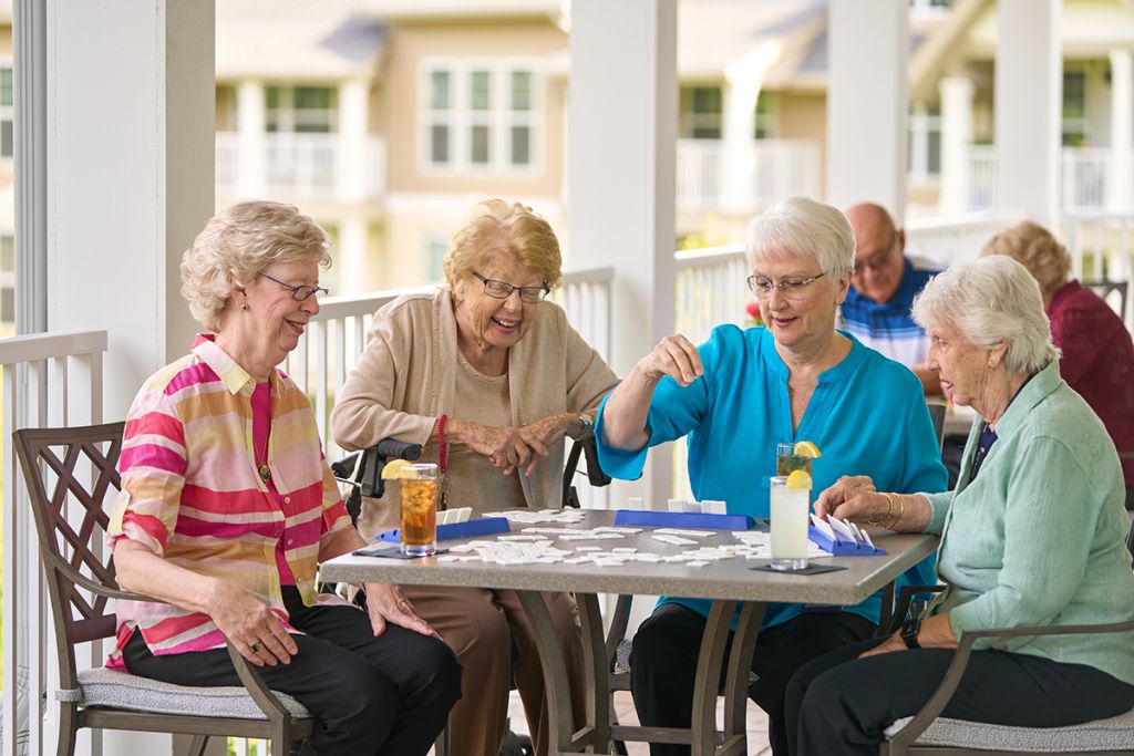 A group of four women playing a tile game at a square table on an outdoor patio at The Vista in Wyckoff, New Jersey