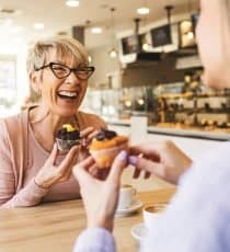 Smiling women talking over cupcake and coffee.