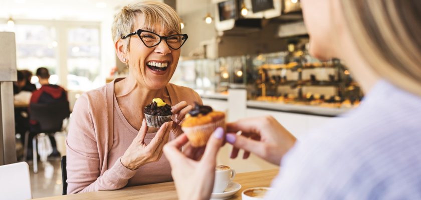 Smiling women talking over cupcake and coffee.