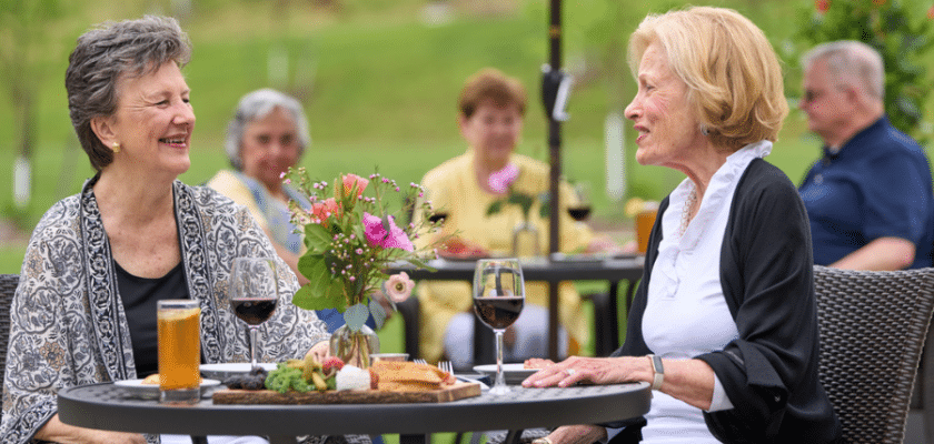 two ladies sitting outdoors at a table with wine